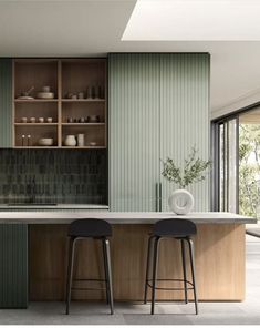 two stools sit in front of an island counter with green cabinets and glass doors