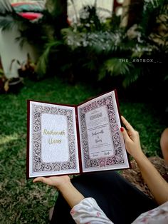 a woman is holding an open book in her hands while sitting on the grass outside