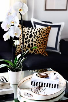 a living room with black couches and white orchids in a vase on the coffee table