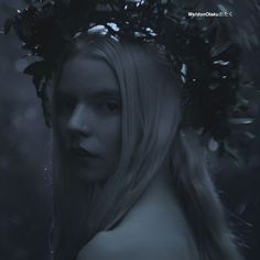 a woman with long blonde hair wearing a wreath of leaves on her head in the dark