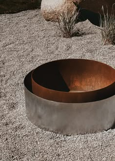 a large metal bowl sitting on top of a gravel covered ground next to grass and rocks