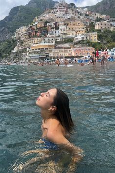 a woman is swimming in the ocean with buildings on top of a hill behind her