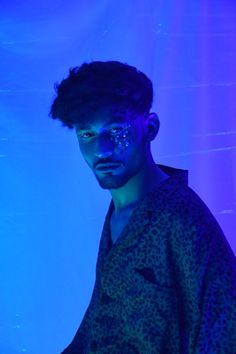 a man with blue light on his face standing in front of a purple and blue background