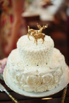 a wedding cake decorated with white roses and gold deer figurines on the top