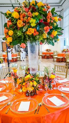 an orange and yellow table setting with flowers in a vase