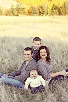 a family is sitting in the tall grass and posing for a photo with their baby