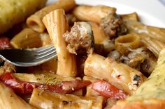 a plate full of pasta and sausage with a fork stuck in the top one side