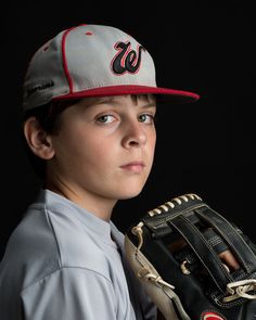 a young boy in a baseball uniform holding a catchers mitt and looking at the camera