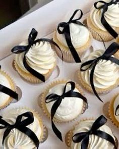 twelve cupcakes with white frosting and black ribbons