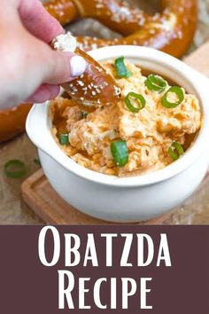 a person dipping something into a bowl with green onions and cheese on top in front of pretzels