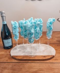 three wine glasses filled with blue cotton swizzles next to a bottle of champagne