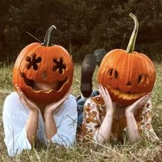 two people laying in the grass with pumpkins on their heads