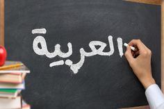 a person writing arabic on a blackboard with books and an apple in the background