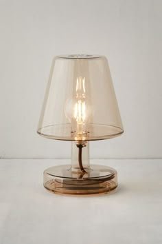 a clear glass table lamp with a gold base and a light bulb in the middle