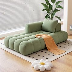 a green couch sitting on top of a wooden floor next to a potted plant