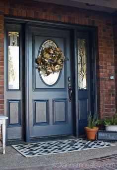 a black front door with a wreath on it and two potted plants in the foreground