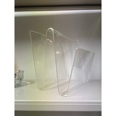 two clear acrylic cases sitting on top of a white shelf next to a glass cup