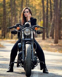 a woman sitting on top of a motorcycle in the middle of the road with trees behind her