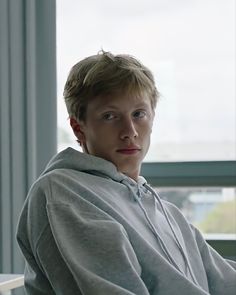 a young man sitting in front of a window with his hands on his hips and looking at the camera