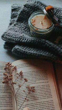 an open book sitting on top of a wooden table next to a glass jar filled with liquid