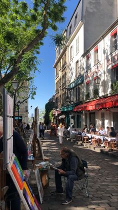 an artist is painting on the street in front of some buildings with people sitting at tables