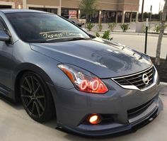 the front end of a gray car parked in front of a building with a sign on it