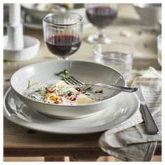 a white bowl filled with food on top of a wooden table next to wine glasses