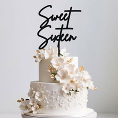 a white wedding cake with flowers on top and the words sweet sixteen written in black