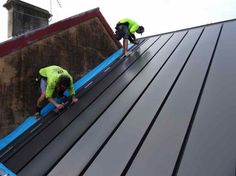 two men working on the roof of a building with metal sheets and blue tarps