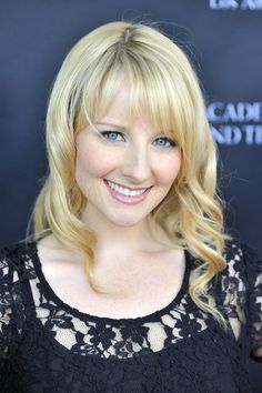 a woman with blonde hair and blue eyes smiling in front of a black background wearing a lace top