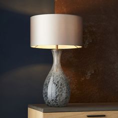 a table lamp sitting on top of a wooden dresser next to a wall with a painting behind it