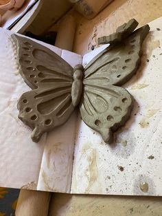 a clay butterfly sitting on top of a piece of paper with holes in it's wings