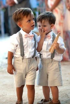 two young boys standing next to each other on a dirt road with people in the background