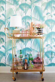 a bar cart with drinks and condiments on it in front of a tropical wallpaper