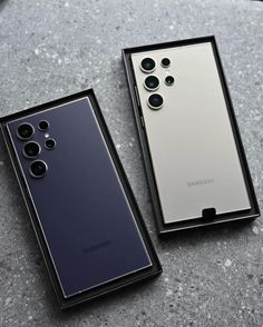 two samsung phones sitting side by side on top of a stone surface, one in silver and the other in black