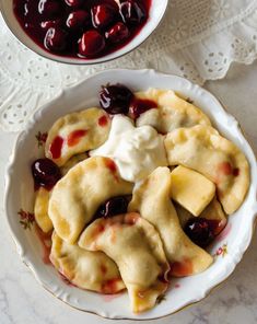 a white plate topped with dumplings covered in cheese and cherry sauce next to a bowl of cherries