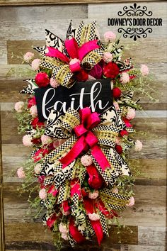 a wreath with the word faith on it and pink flowers is hanging in front of a wooden wall