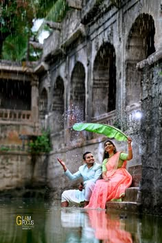 a man and woman sitting on steps under an umbrella in the rain, with water splashing over them