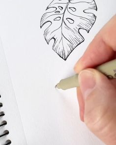 a person is drawing a leaf on paper with a marker and pen in their hand