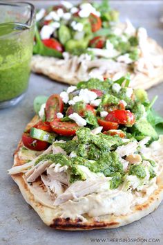 two pita breads topped with chicken, veggies and pesto sauce