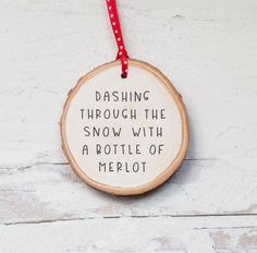 a wooden ornament hanging on a red ribbon with the words dashing through the snow with a bottle of merlot