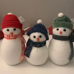 three snowmen wearing hats and scarves are sitting on a counter top, one has a scarf around his neck