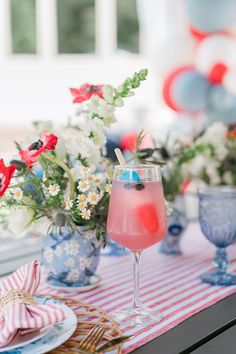 a table topped with drinks and flowers on top of a red white and blue table cloth