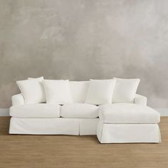 a white sectional couch with pillows on the top and bottom, in front of a gray wall