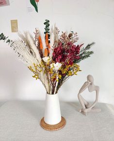 a white vase filled with lots of flowers on top of a table next to a figurine