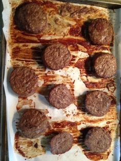 some meat patties are sitting on top of a sheet of parchment paper in an oven