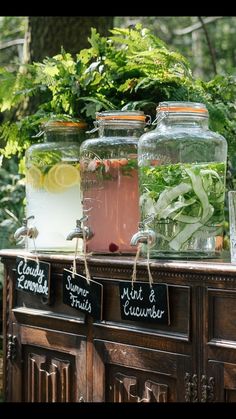 three jars filled with water and plants on top of a wooden table in the woods