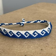 a blue and white braided bracelet sitting on top of a wooden table next to a wall