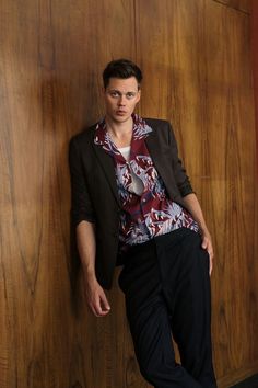 a young man leaning against a wooden wall