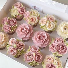 twelve cupcakes with pink and white frosting roses in a box on a table